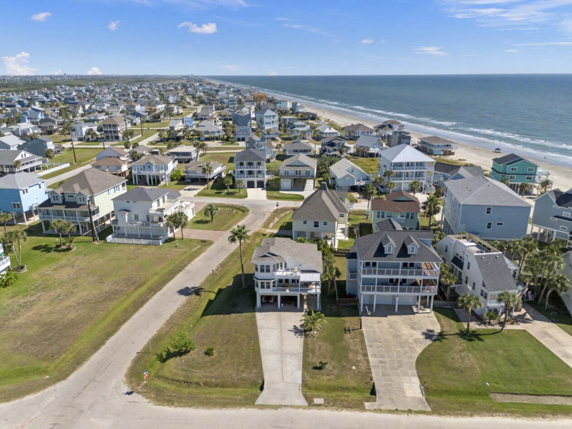 Aerial view of a coastal neighborhood with houses along the beach and the ocean in the background.