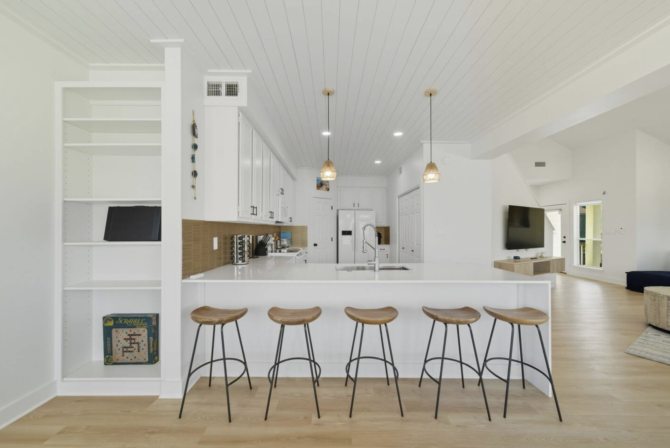 Modern open-concept kitchen and living area with white cabinets, wooden accents, and a breakfast bar with five wood and metal stools