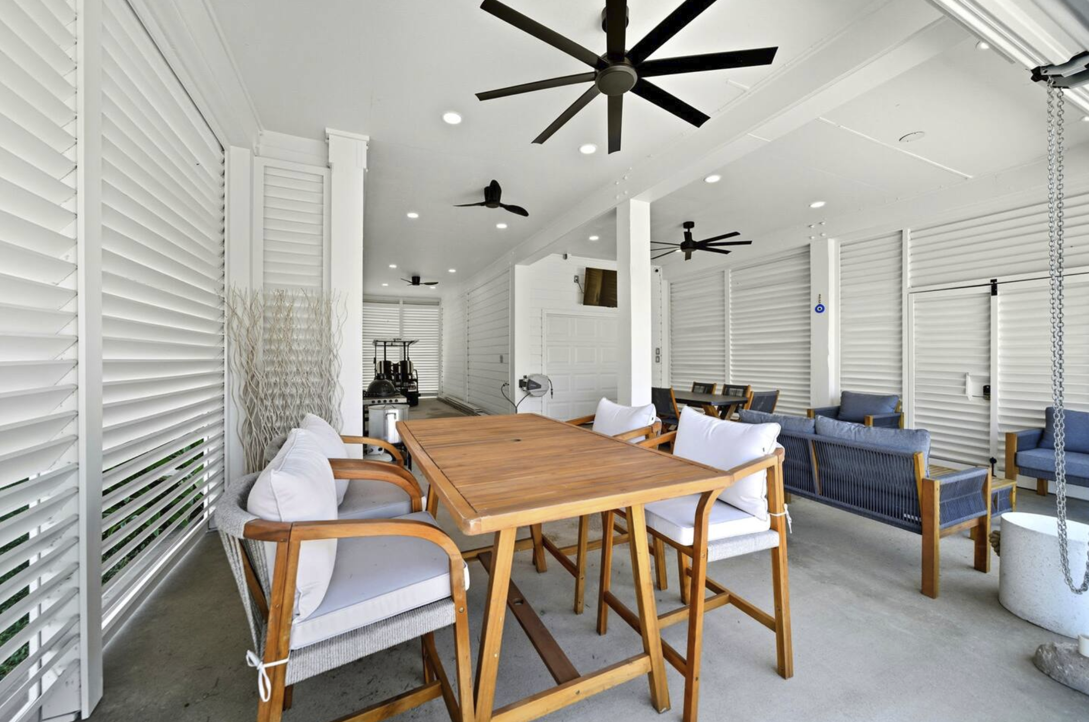 Indoor lounge area with wooden tables, white and blue cushioned chairs, ceiling fans, and modern decor.