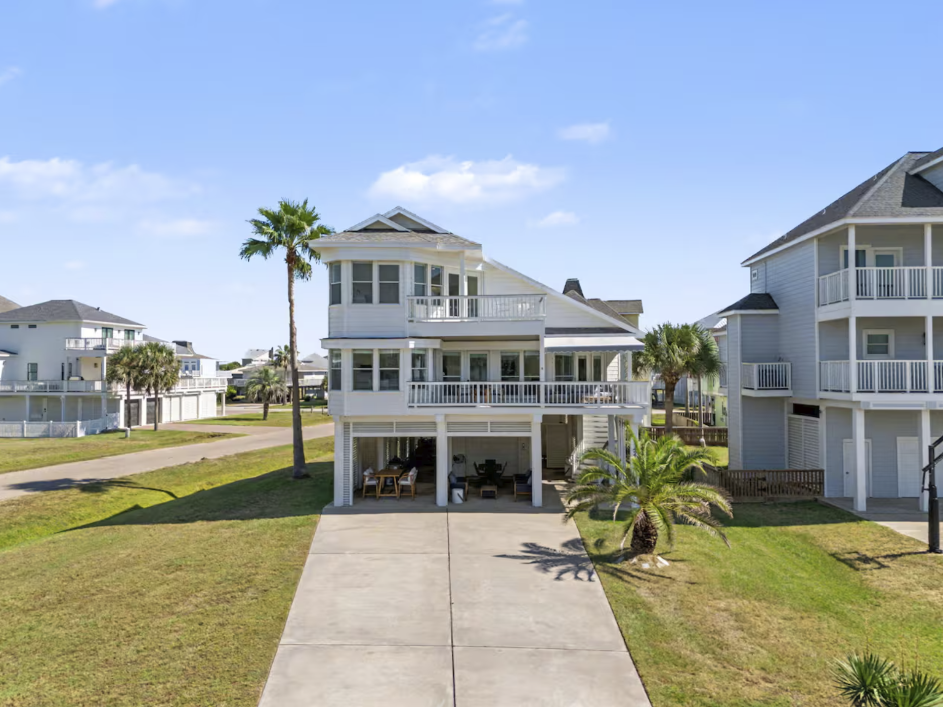 A coastal home with multiple porches and large windows, surrounded by a well-kept lawn and palm trees, under a bright blue sky.