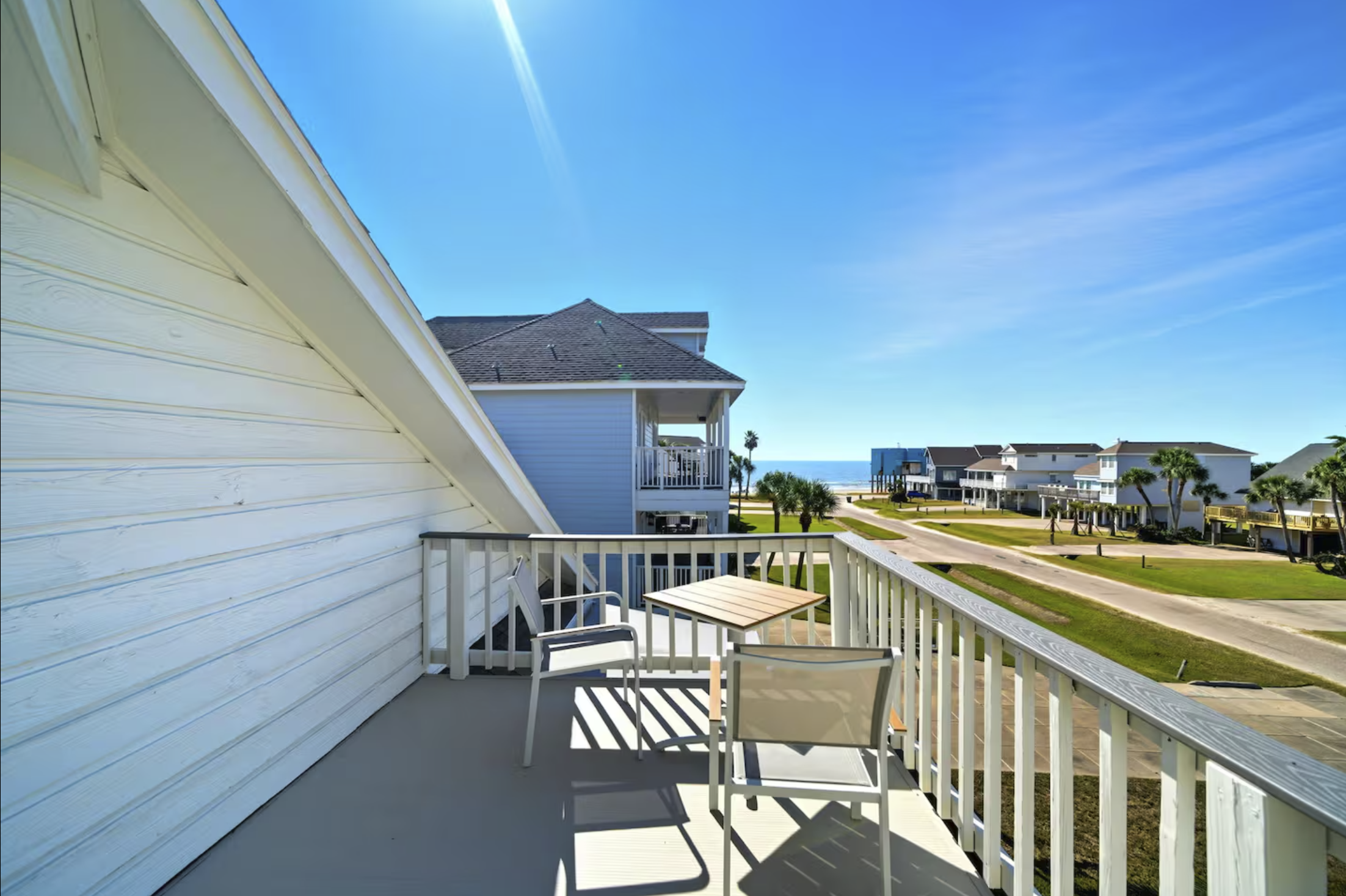 Balcony view of beach houses with ocean in the background, clear blue sky, and palm trees.