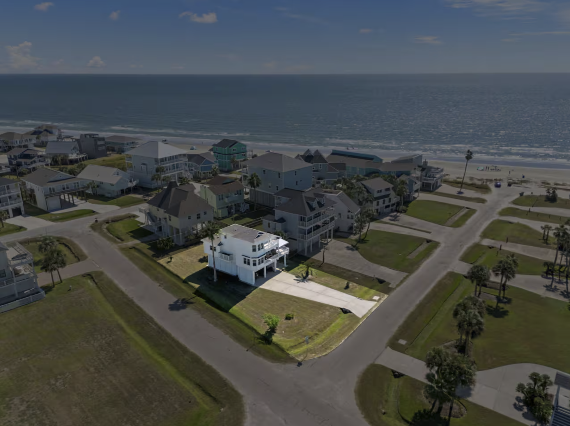 Aerial view of a coastal neighborhood with houses near the beach and the ocean in the background.
