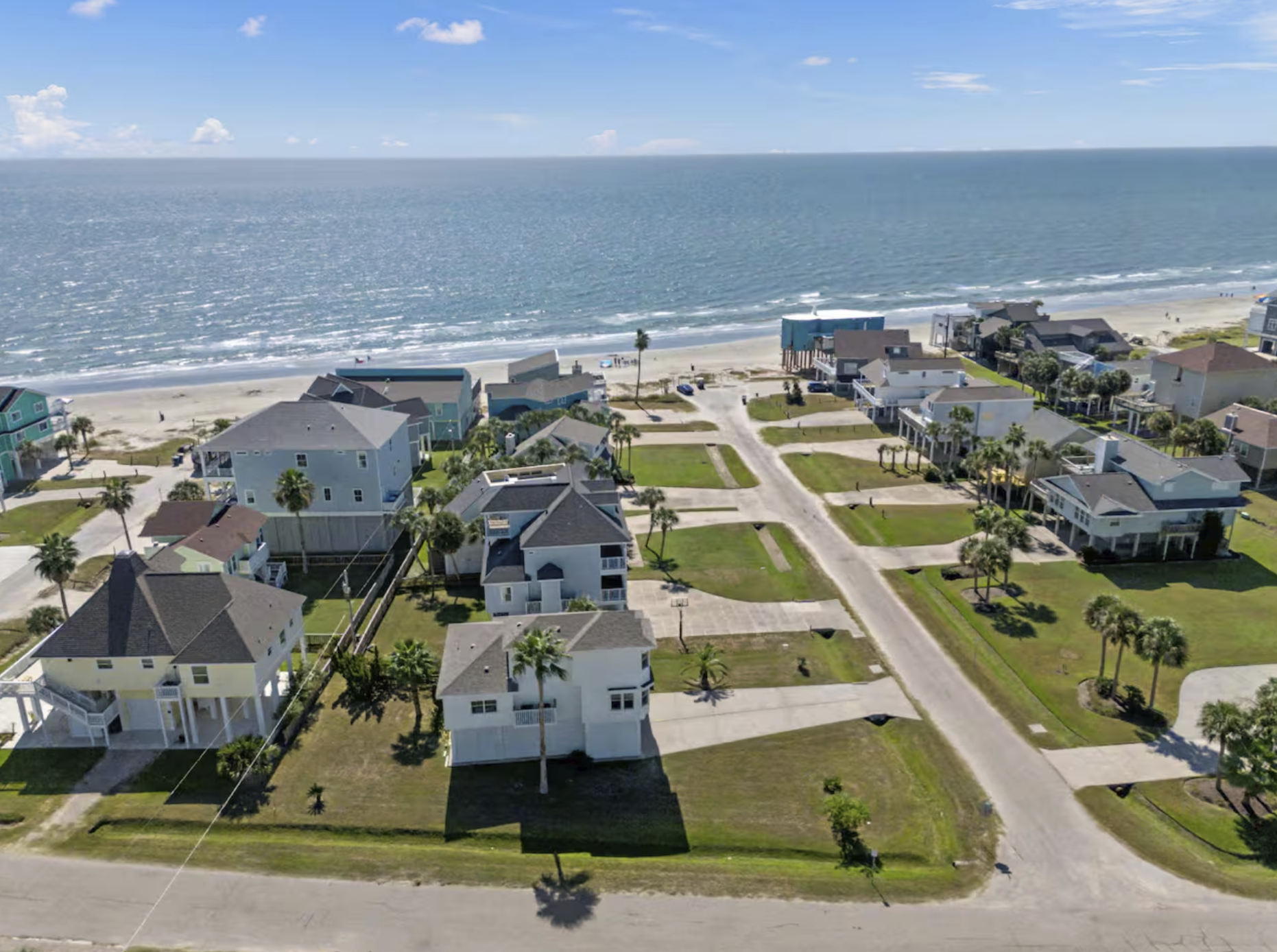 Aerial view of a beachside neighborhood with houses, palm trees, and a sandy beach leading to the ocean.