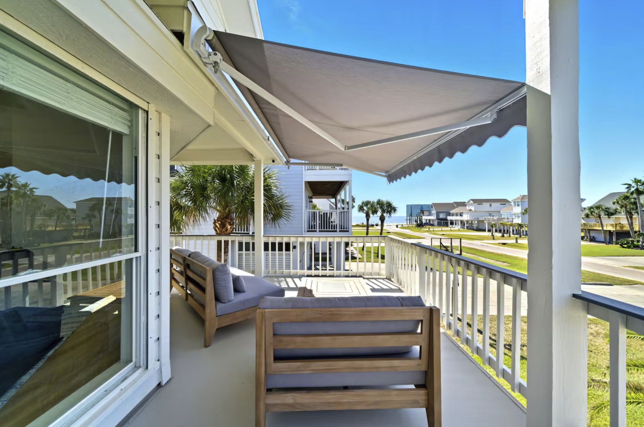 View from a porch overlooking a neighborhood with beach houses, palm trees, and a clear blue sky.