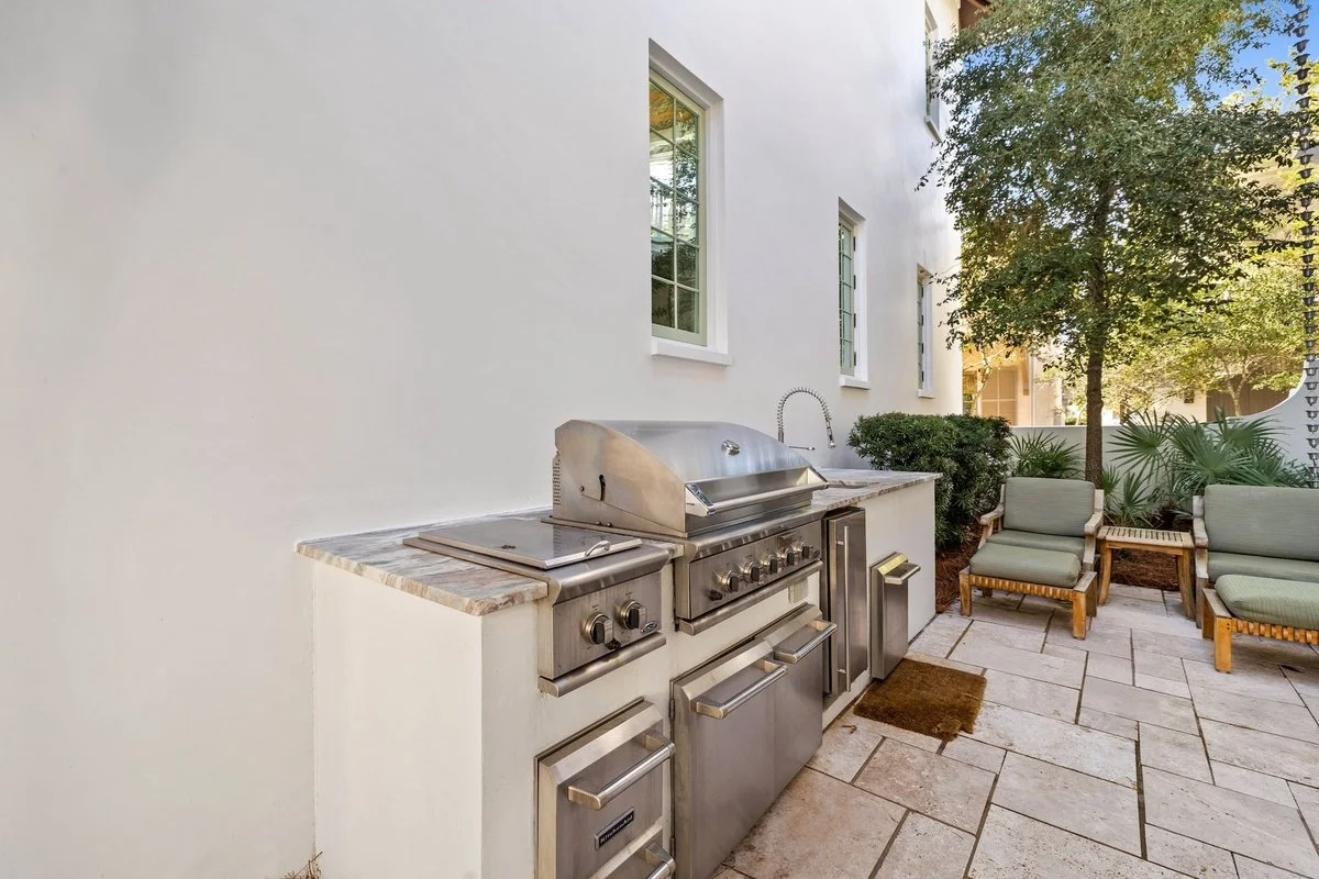 Outdoor patio area with a stainless steel grill, patio furniture, and green plants.