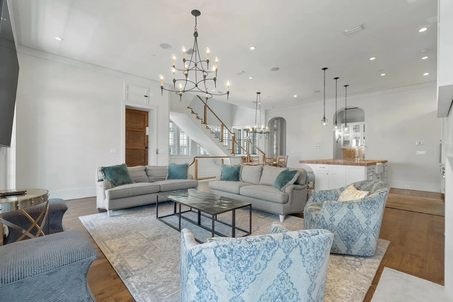 Living room with two light gray sofas, patterned armchair, coffee table, area rug, and pendant lighting, with a staircase in the background.