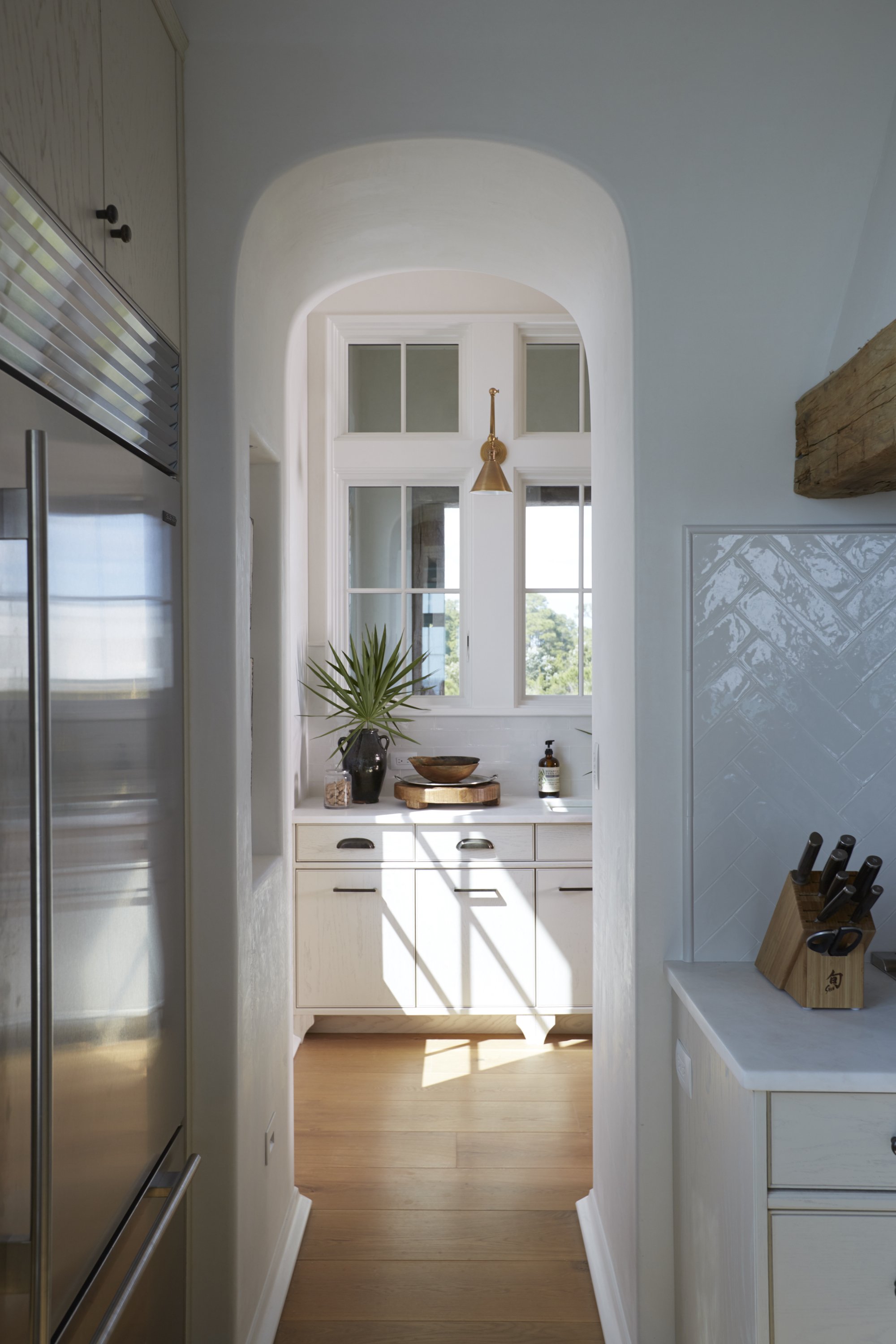 A bright kitchen with white cabinetry, a window with sunlight streaming in, and a countertop with decorative items including a potted plant, a bowl, and a soap dispenser.