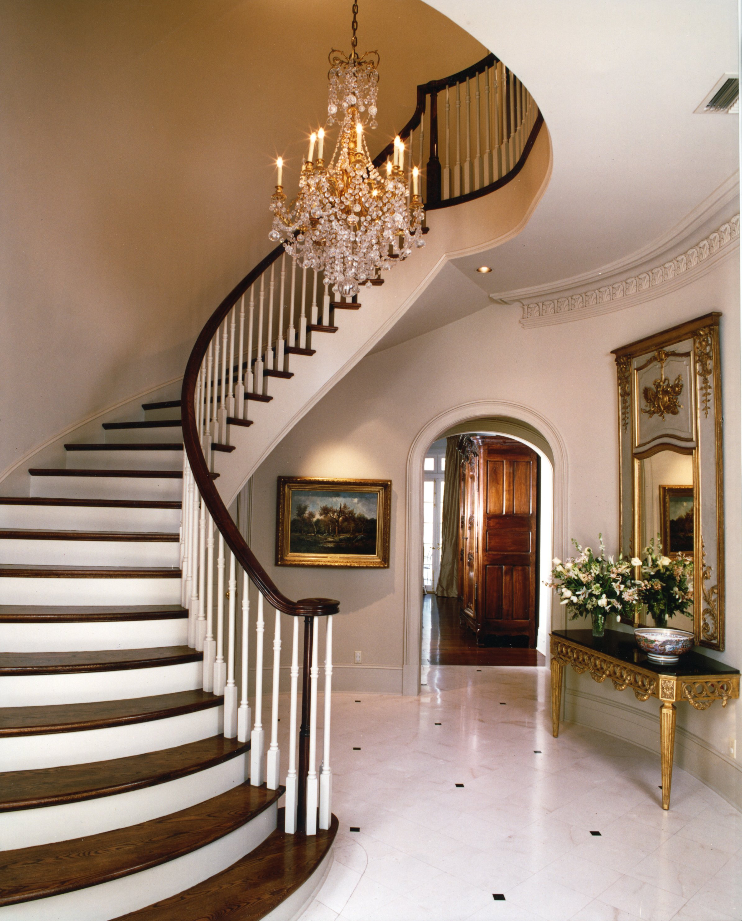 Interior of a luxurious home with a grand staircase, crystal chandelier, and elegant decor.