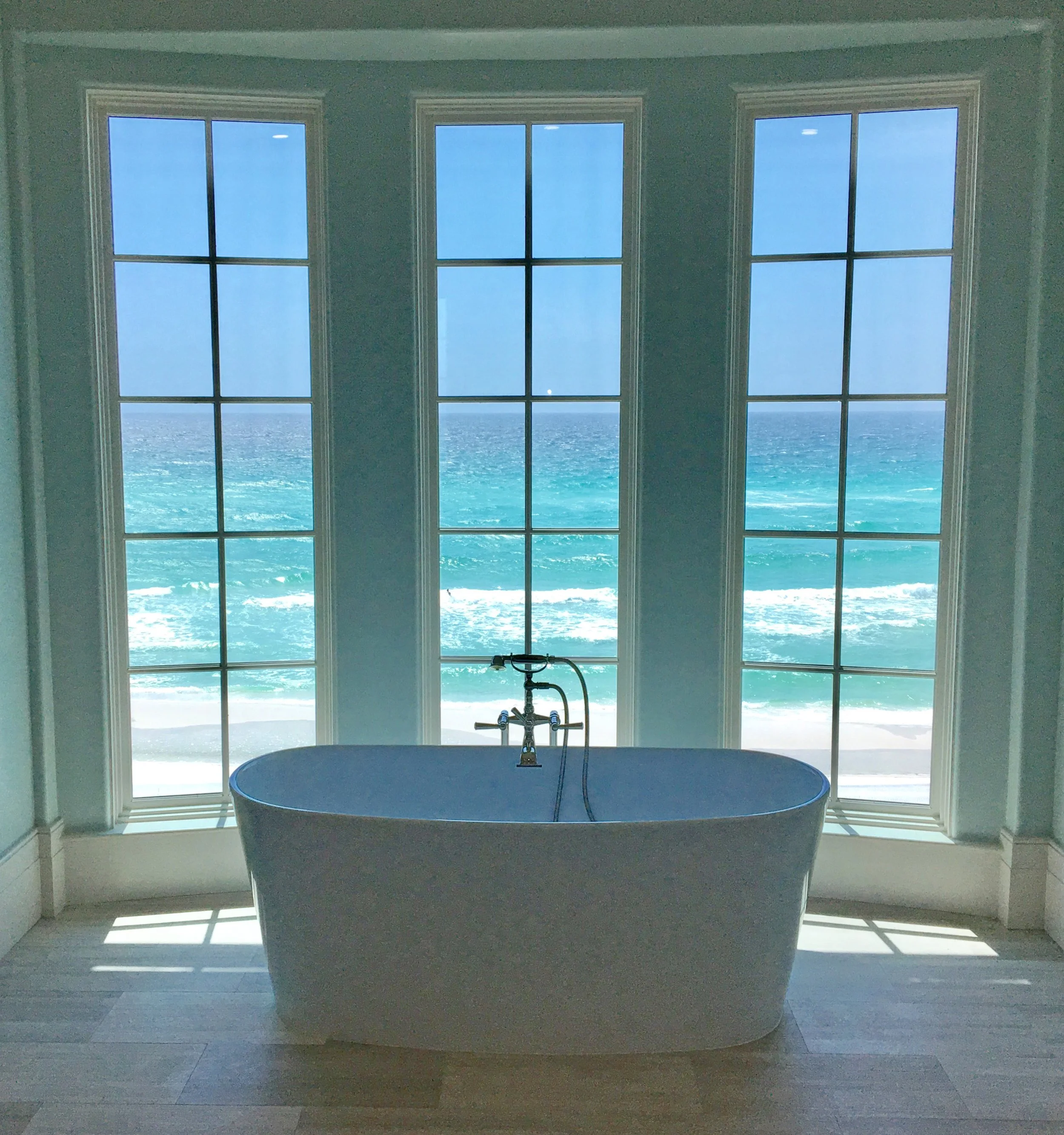 A freestanding bathtub in front of large windows overlooking the ocean.
