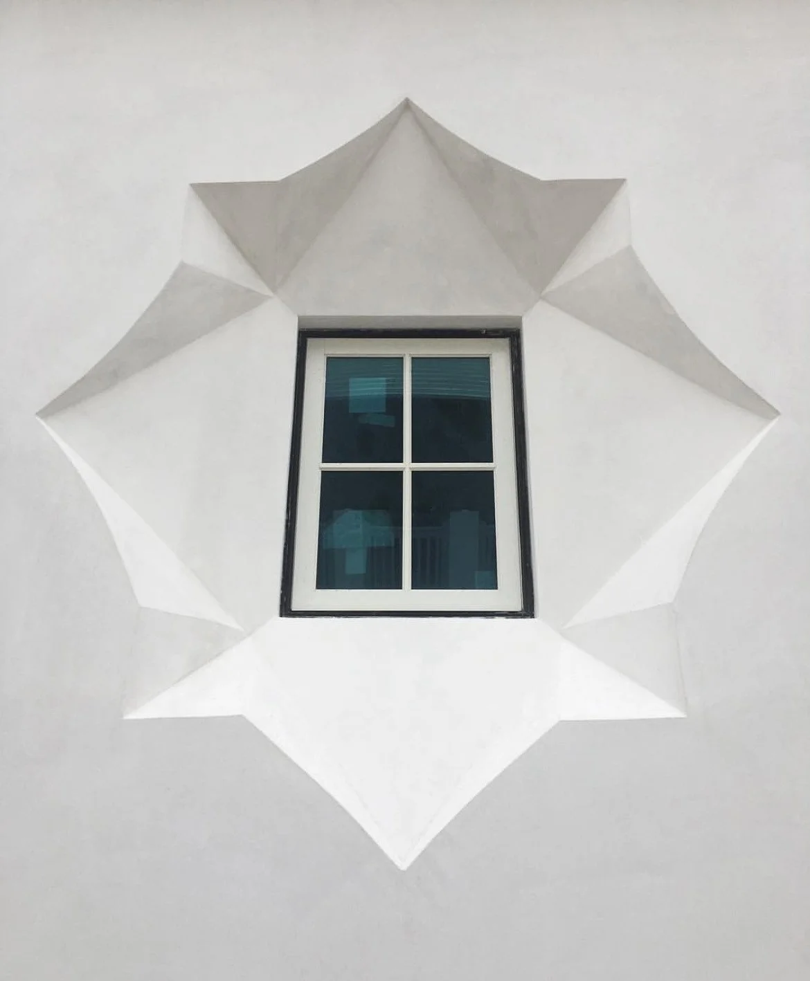 A window on a white wall with a decorative white paper surround shaped like a star.