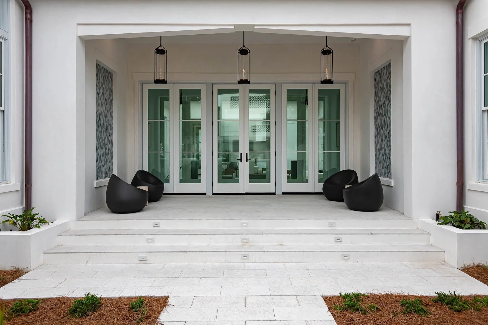 Front porch with white steps, black modern chairs, glass door entrance, and hanging lantern lights.