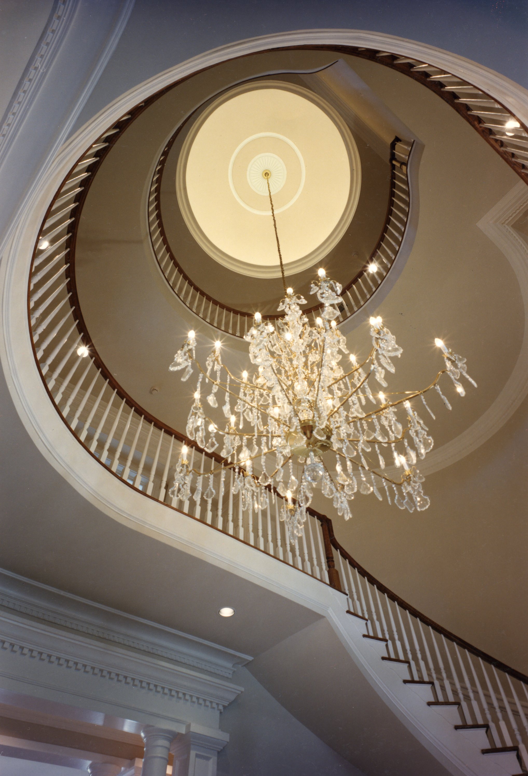 Elegant chandelier hanging from a spiral stairwell ceiling in a luxury home.