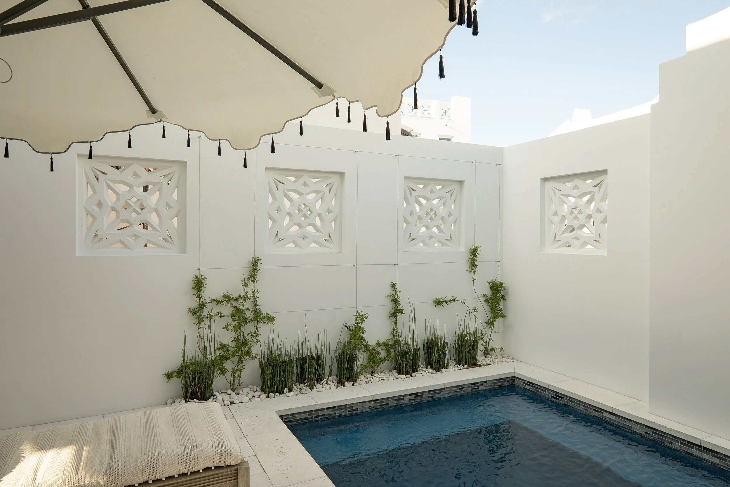 Small outdoor pool in a white enclosed patio with decorative wall panels and greenery