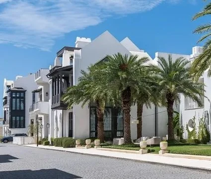 White modern residential buildings with palm trees and a paved street under a blue sky.