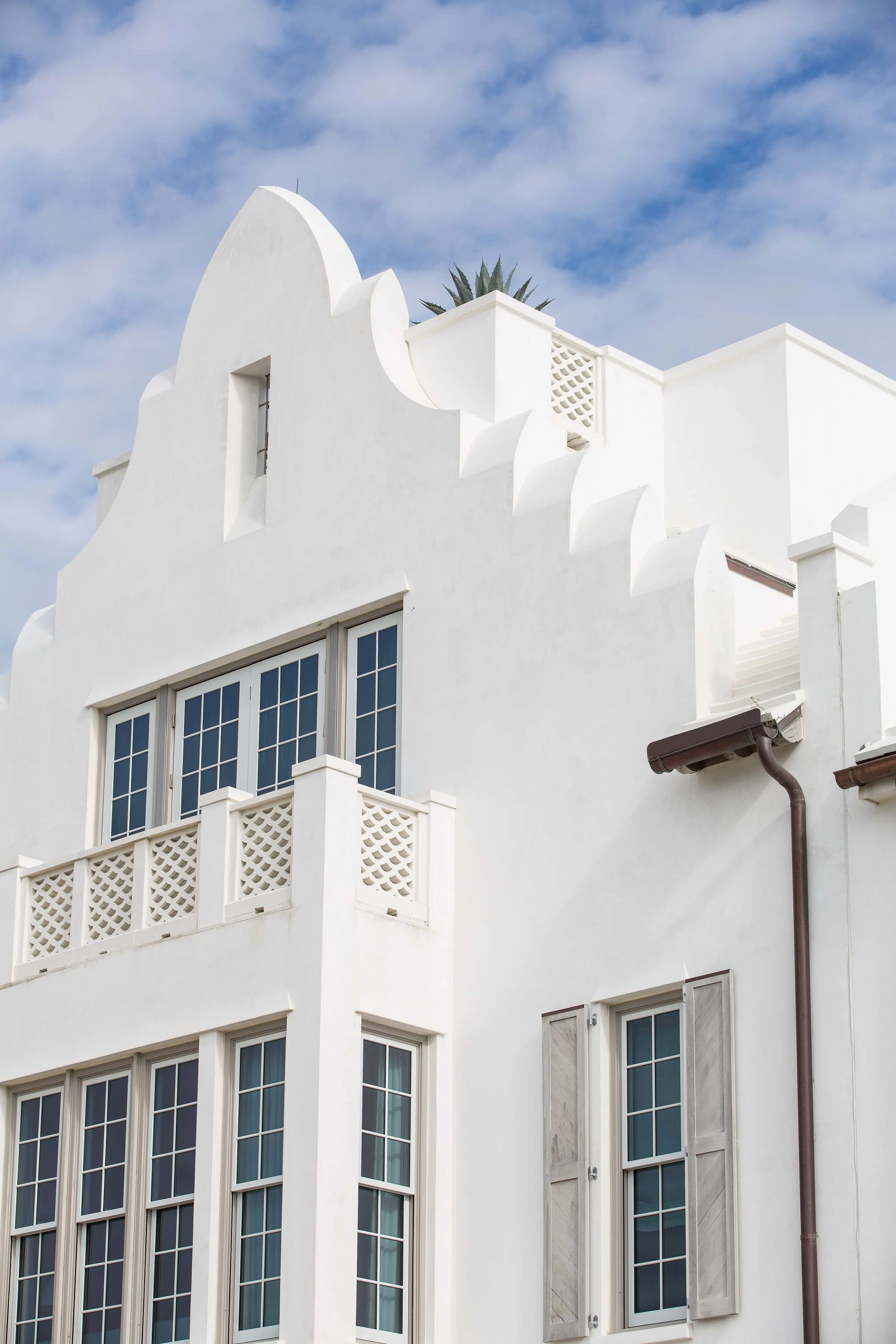 White building with a decorative rooftop, large windows, and a brown gutter, set against a partly cloudy sky.