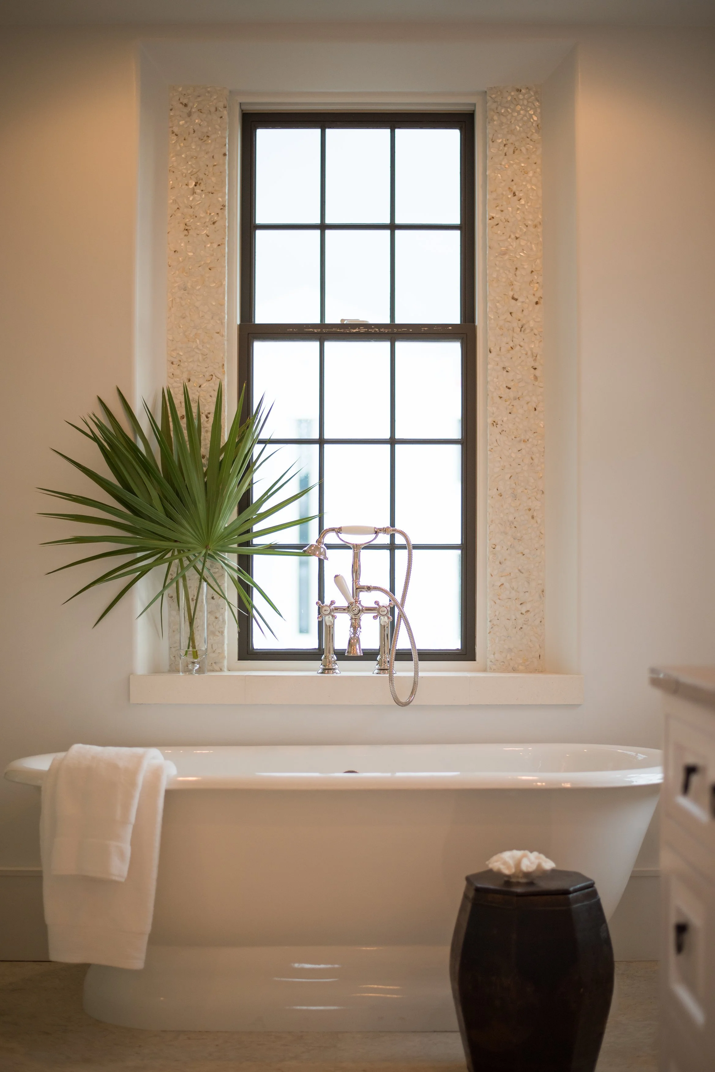 Bathroom with a freestanding bathtub, a large window, a green plant in a vase, and a towel draped over the tub.
