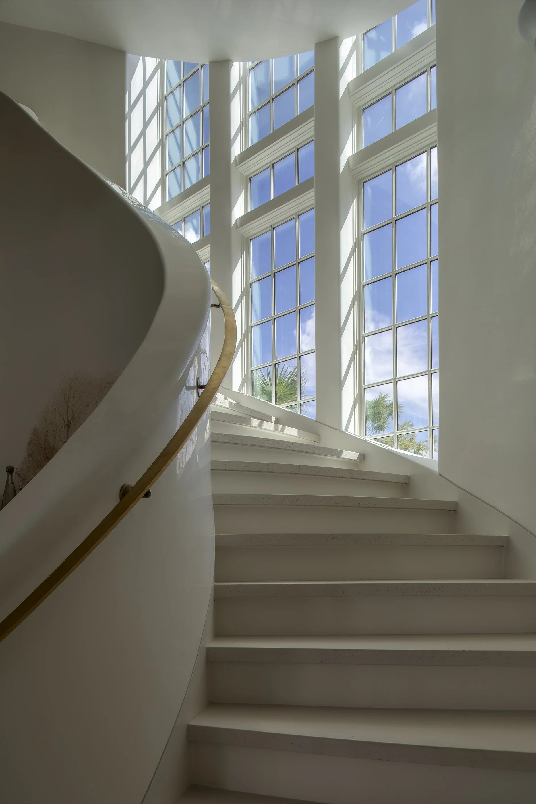 Indoor staircase with large windows showing blue sky and palm trees outside.