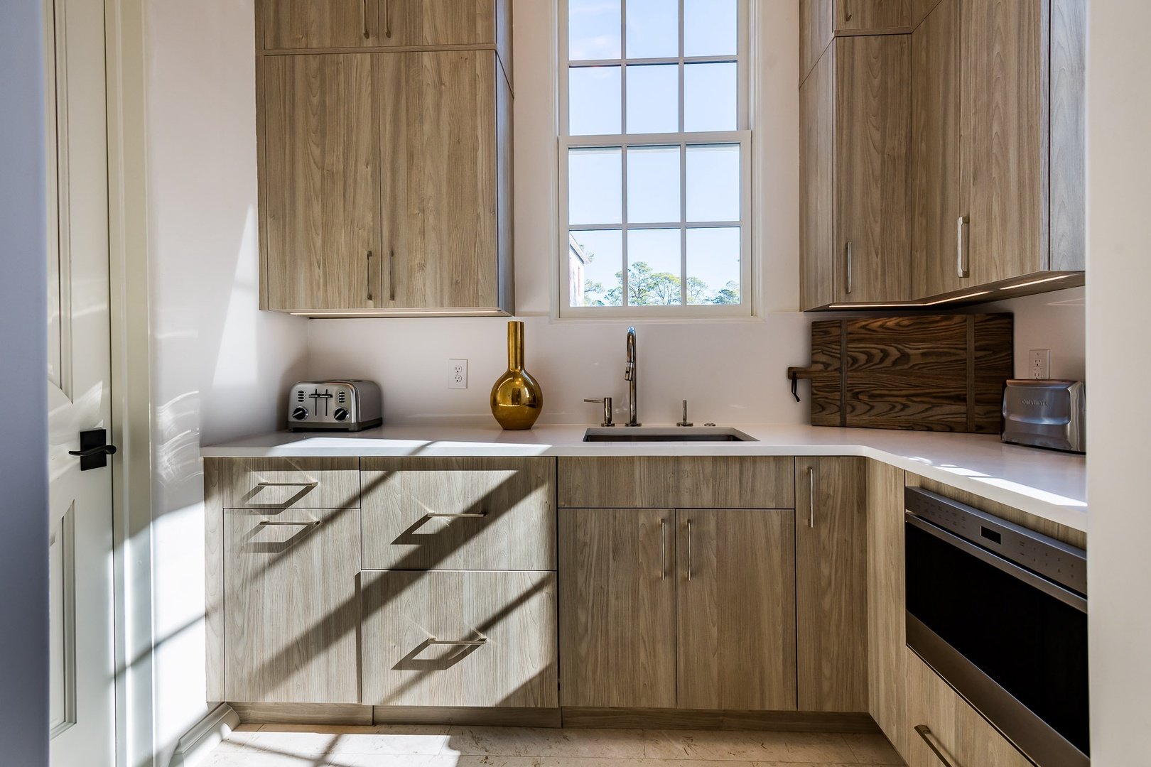 Modern kitchen with light wood cabinets, white countertop, stainless steel appliances, and a large window above the sink letting in natural light.