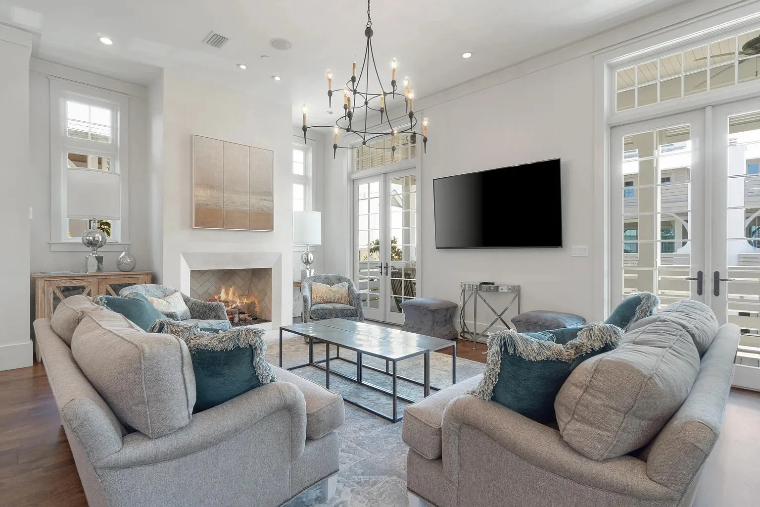 Bright living room with beige sofas, blue pillows, a fireplace, a wall-mounted TV, glass doors, and large windows