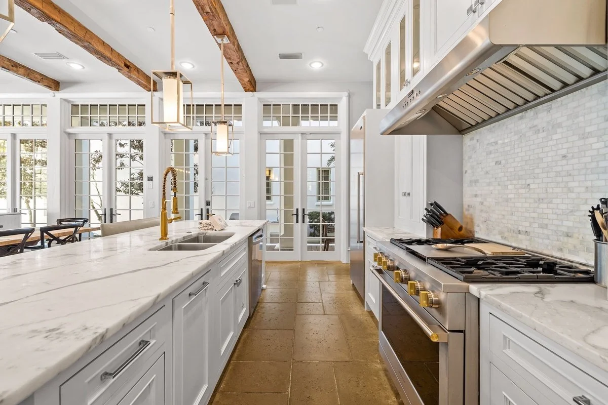 Modern kitchen with white cabinets, marble countertops, a stainless steel stove, and glass-paneled doors leading outside.