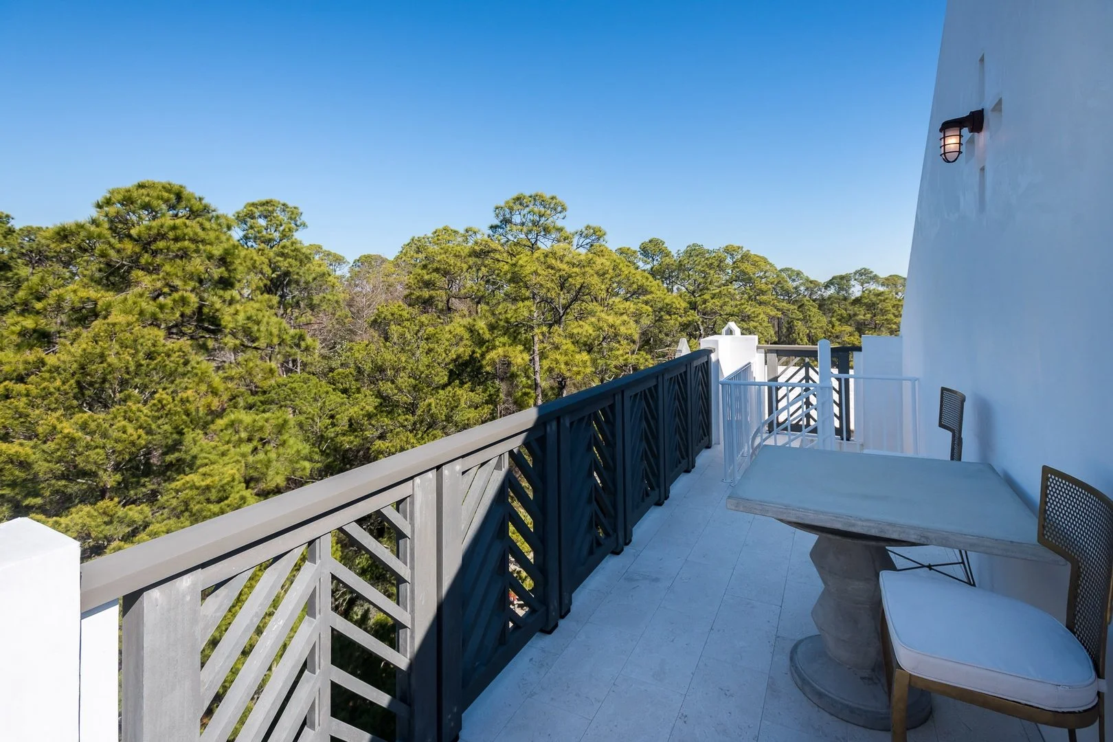 Balcony view with outdoor table and chairs overlooking green trees under a clear blue sky.