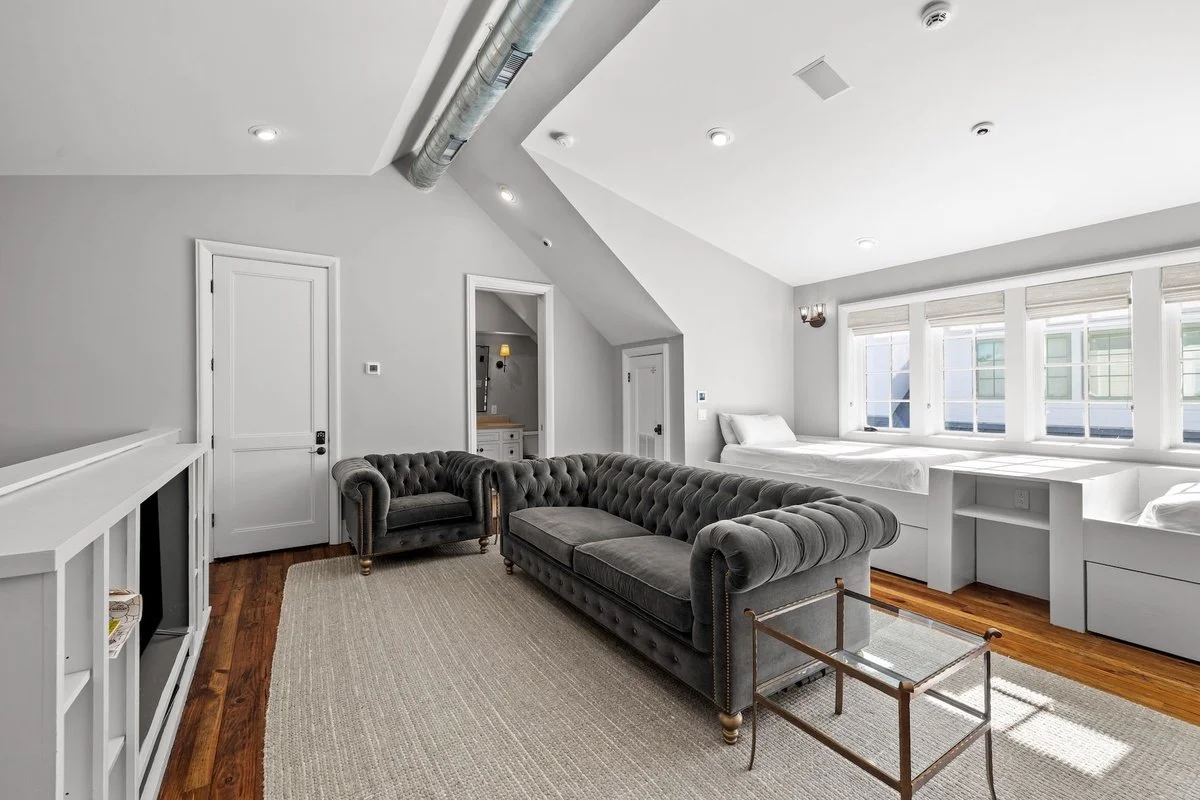 Living room with gray sofas, a beige rug, a window seat with pillows, and white walls.