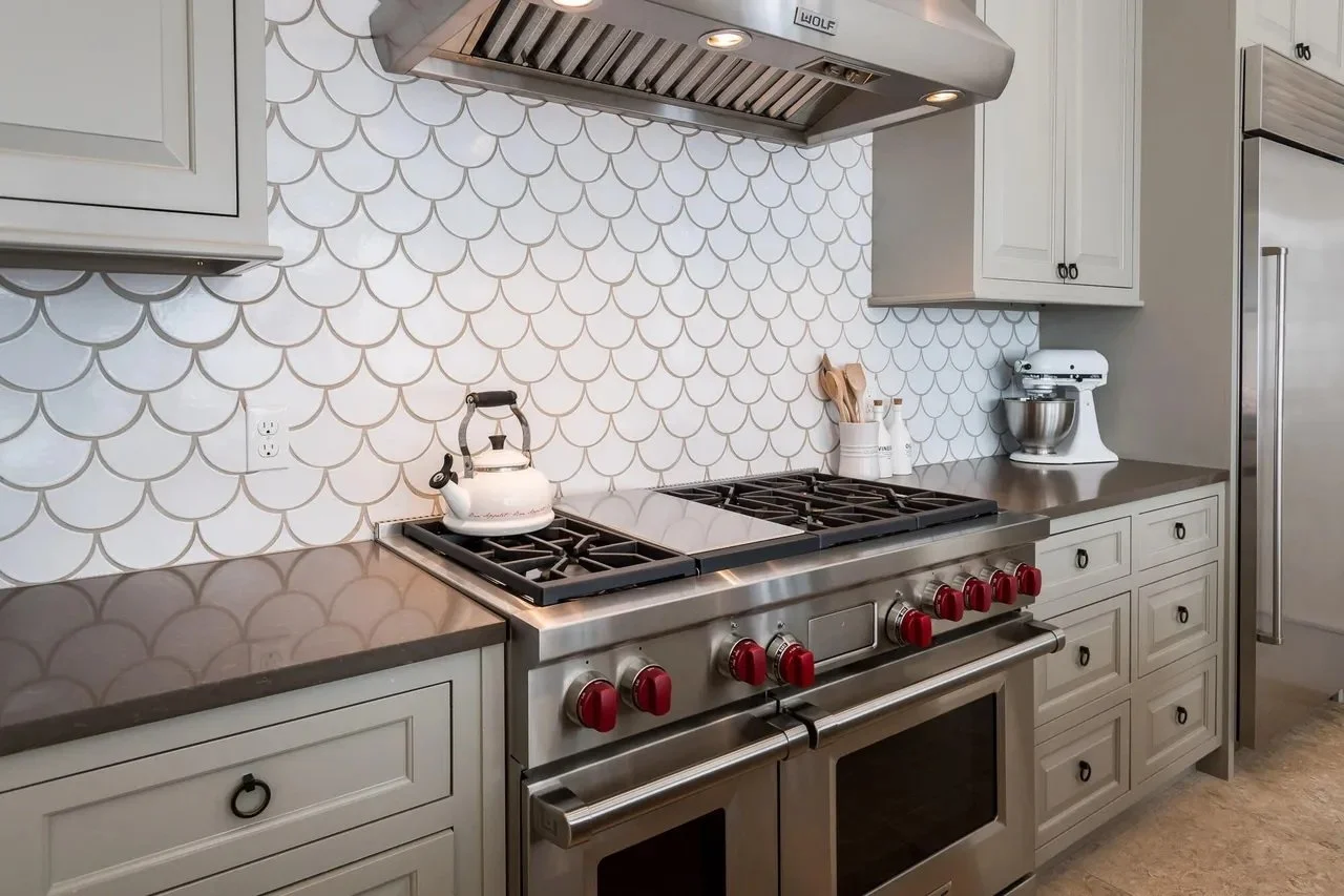Modern kitchen with a stainless steel stove, white cabinets, a patterned backsplash, a vintage teapot, a stand mixer, and cooking utensils.