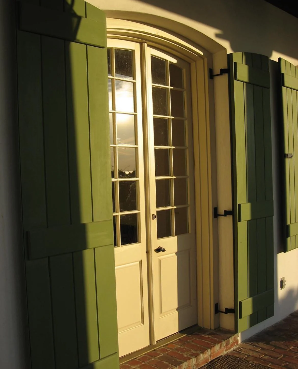 Close-up of a door with green shutters, a glass panel, and brick steps outside.