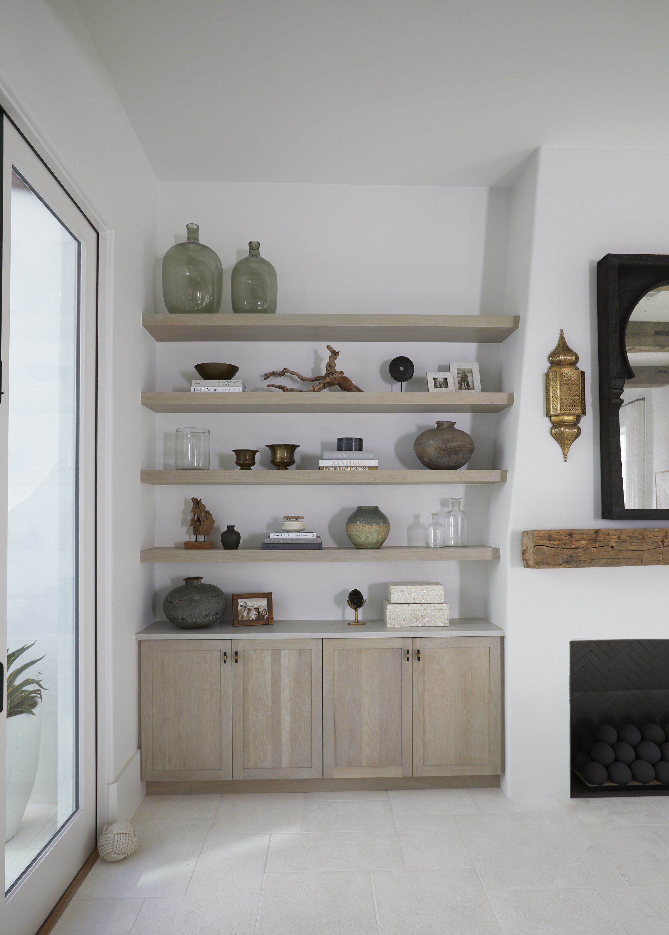 A built-in wooden cabinet with multiple shelves displaying decorative objects, vases, small sculptures, framed photos, and books in a modern, minimalist living room.