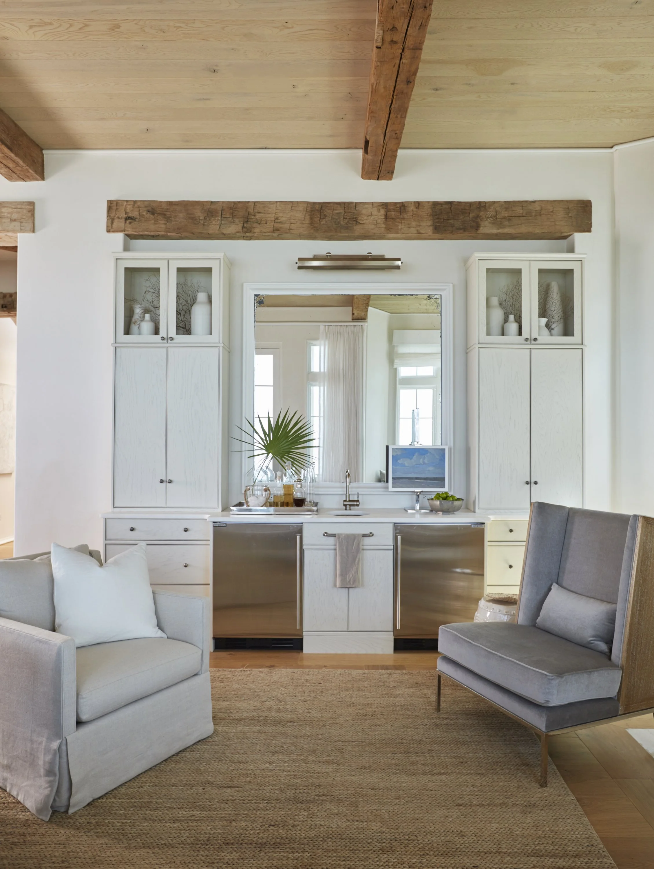 Living room with a small kitchenette, white cabinets, a large mirror, and wooden beams on the ceiling.
