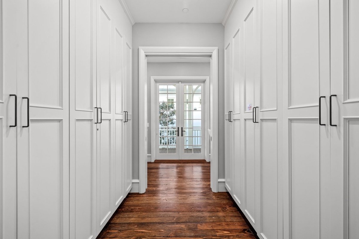 A bright hallway with white paneling on the walls, dark hardwood floors, and glass double doors leading outside.
