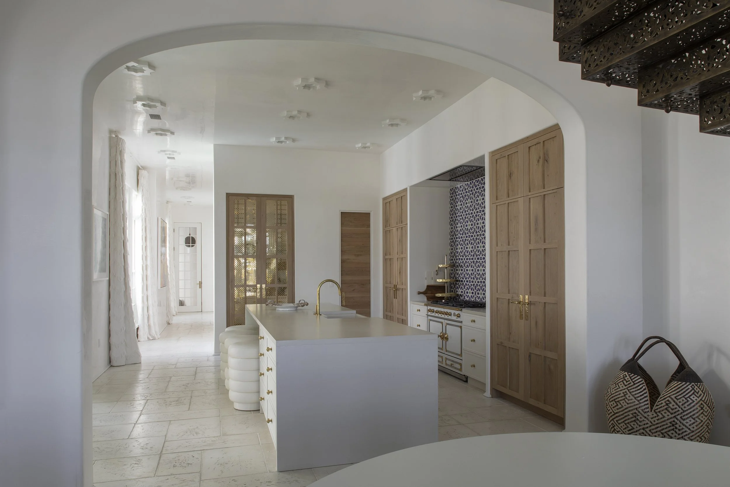 Modern kitchen with white island, gold fixtures, wooden cabinets, patterned tile backsplash, and woven basket on the floor.