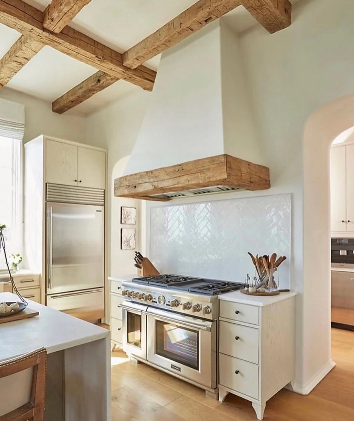 Kitchen with white cabinets, a stainless steel refrigerator, a gas stove with an oven, and wooden ceiling beams.
