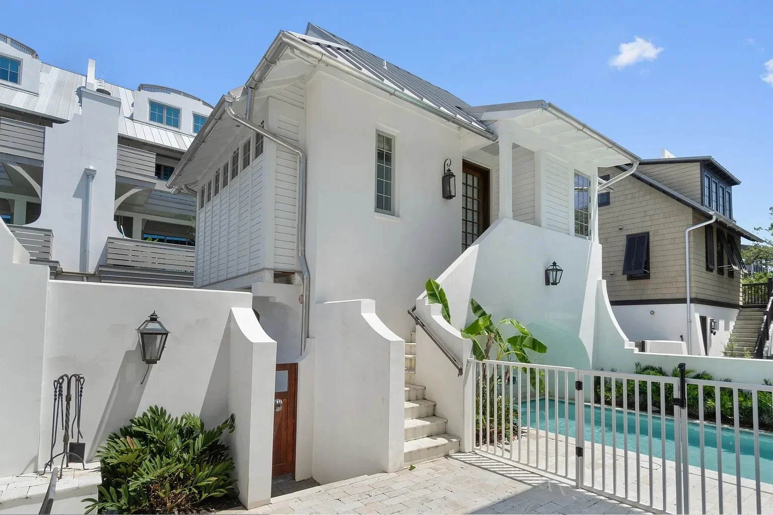 White house with stairs, a small pool, and tropical plants under a clear blue sky.