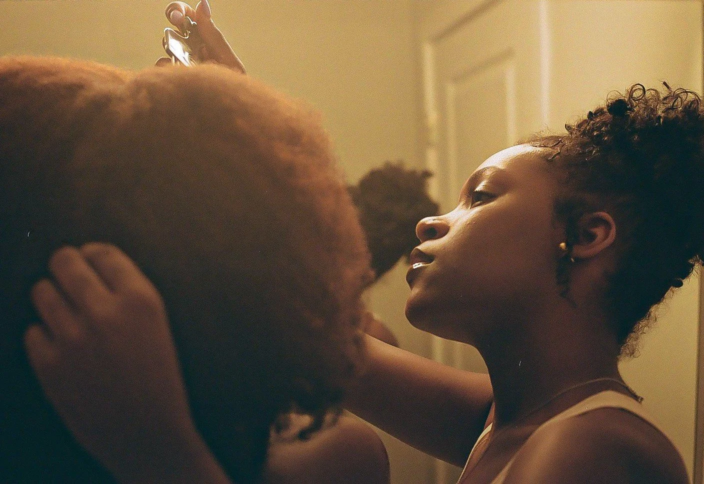 A young woman with short curly hair and earrings looking into the eyes of another person, touching their head.
