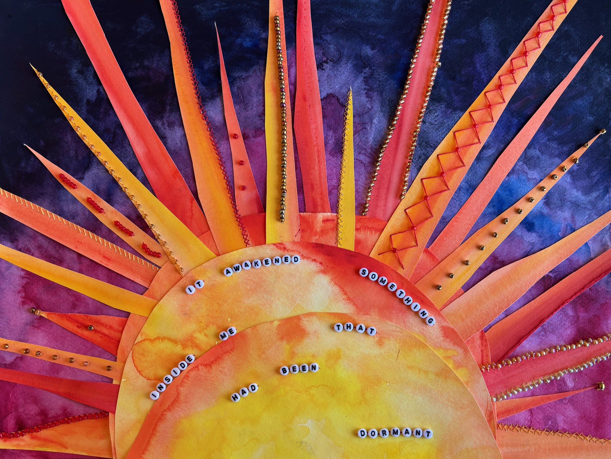 Colorful paper sun with orange and yellow rays and a watercolor sun at the center, featuring a message spelled out with letter beads.