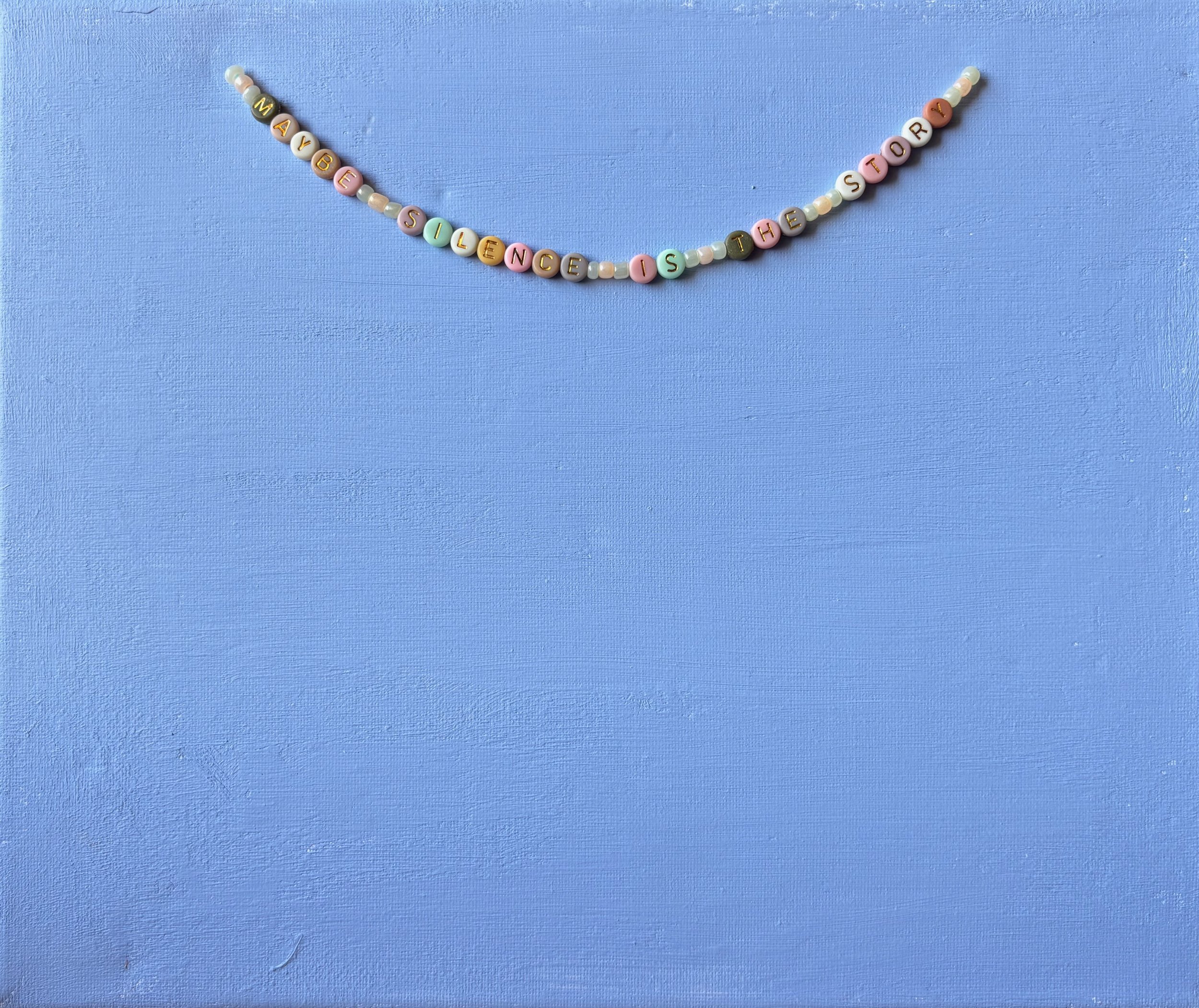 Beaded necklace with colorful letter beads spelling out 'MY BABE'S SILENCE IS THE STORY' hanging against a blue textured background.