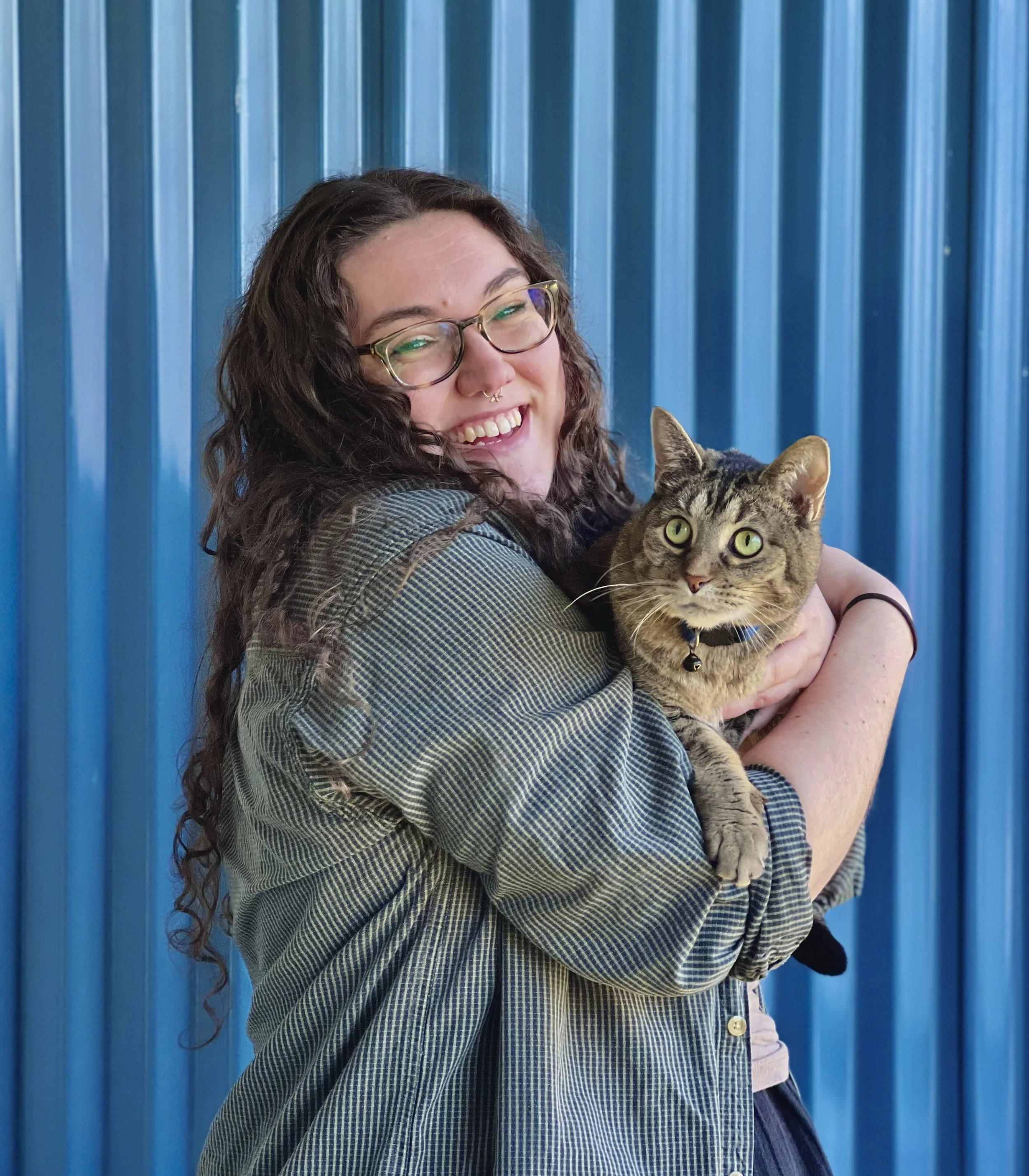 White woman with brown curly hair wearing a green shirt smiling and holding a cat in front of a blue background