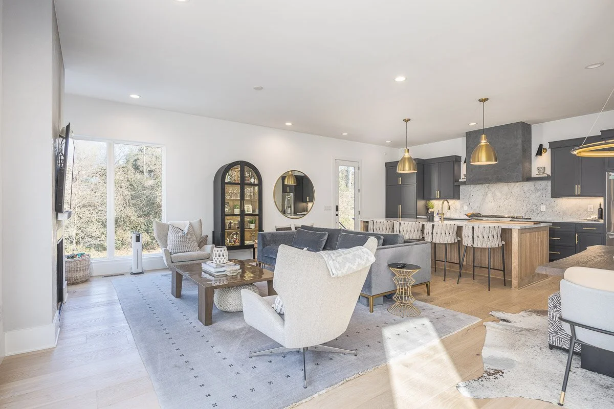 Open-concept living room and kitchen with modern decor, light-colored hardwood floors, and large windows.