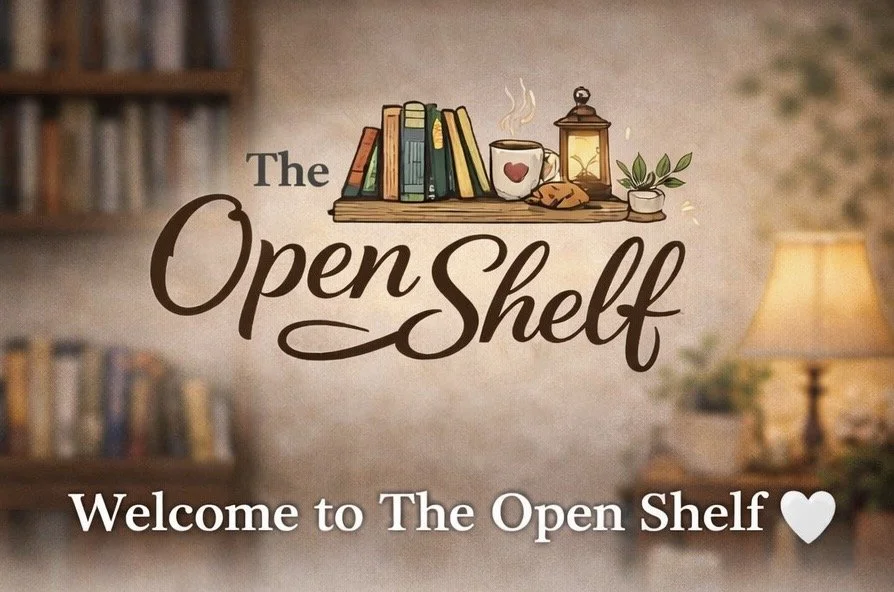 Decorative sign with books, a steaming mug, a lantern, and a small plant, with the words "The Open Shelf" and "Welcome to The Open Shelf" accompanied by a heart symbol.