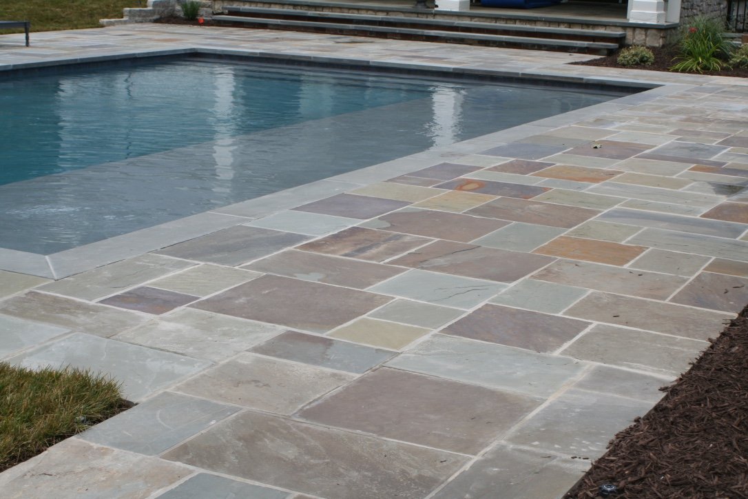 A backyard with a swimming pool and a multi-colored flagstone patio surrounding it.