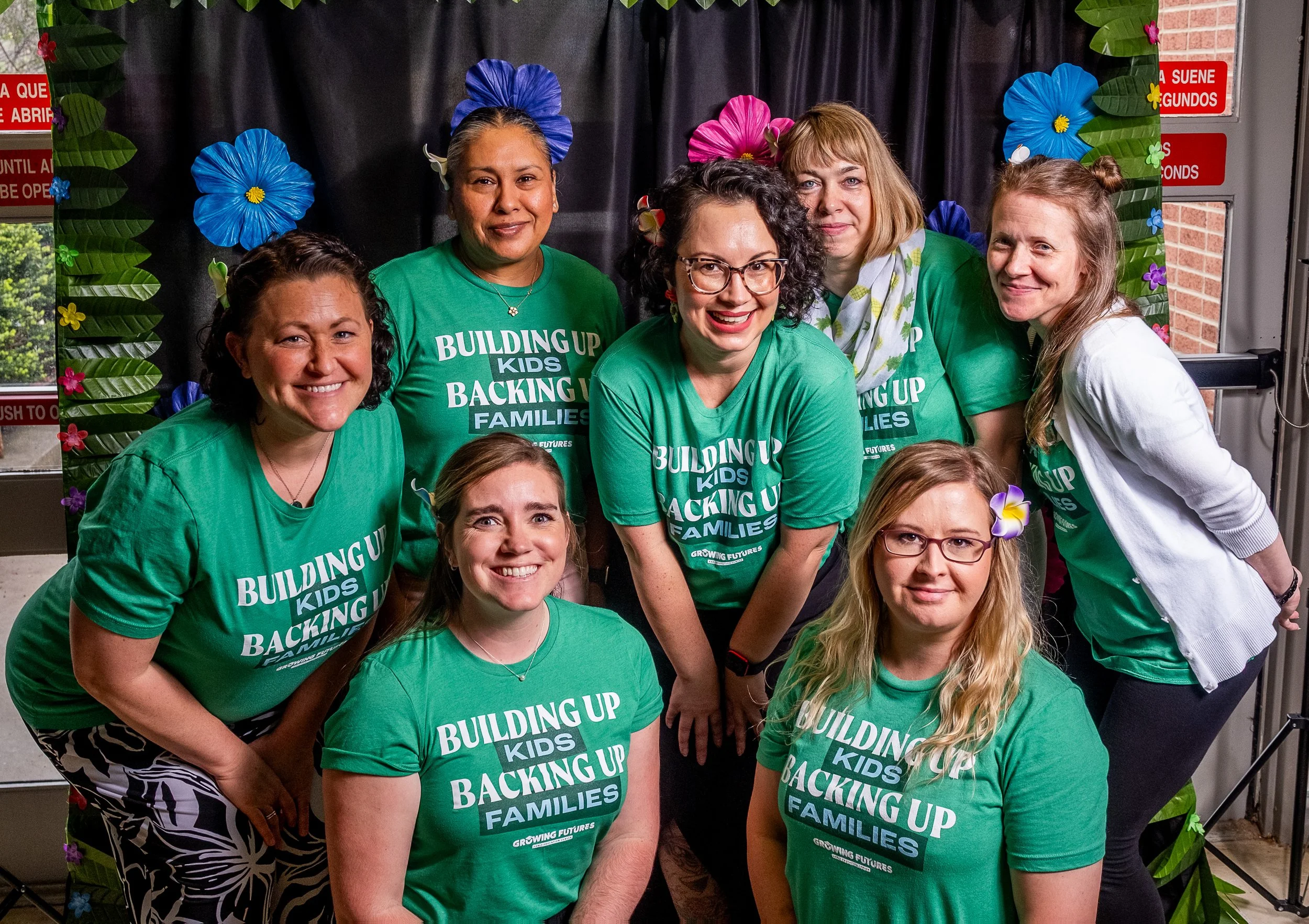 Seven staff members posing in front of floral backdrop.