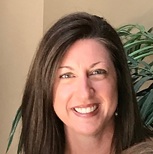 A smiling woman with long dark hair and earrings in front of a plant.