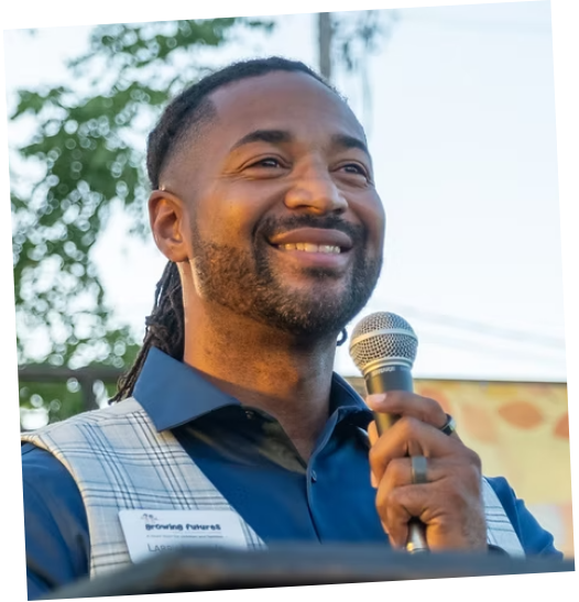 Man smiling and speaking into a microphone outdoors at an event.