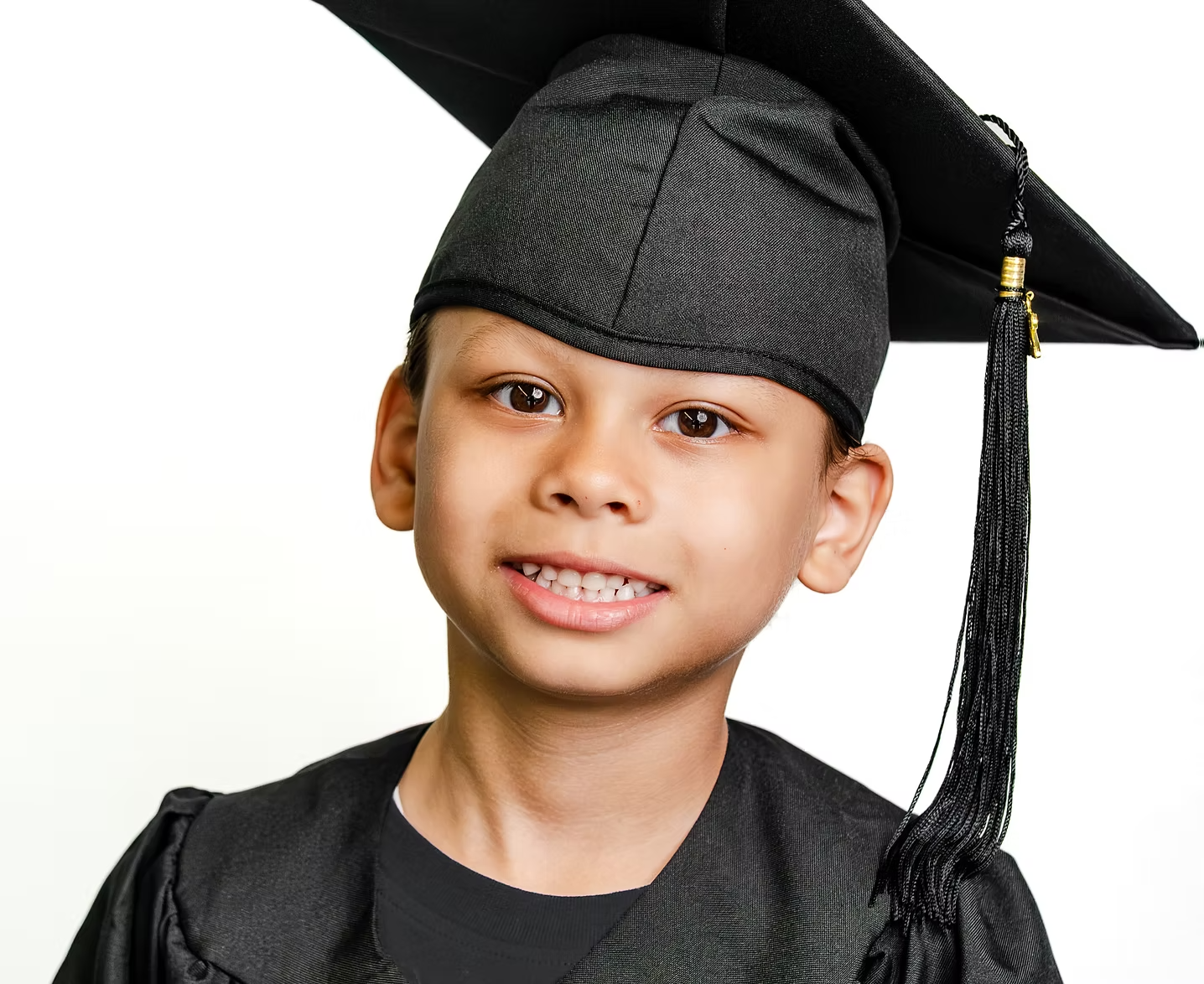 A young boy with a big smile wearing a black graduation cap and gown.