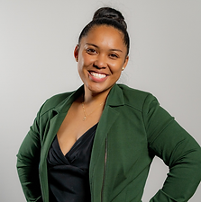 Portrait of a smiling woman with dark hair in a bun, wearing a green blazer and black top, standing against a light gray background.