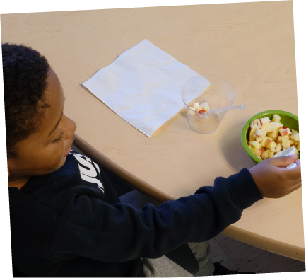 Child reaching for a bowl of chopped fruit at table