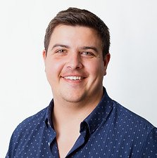 A smiling man with short dark hair wearing a navy blue shirt against a plain white background.
