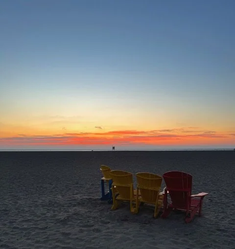 Four colorful beach chairs facing the ocean at sunset.