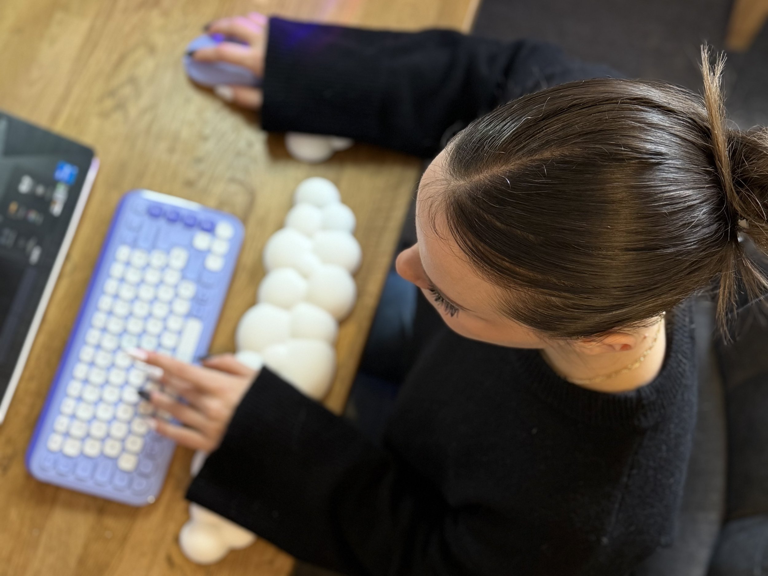 Une femme utilise un clavier d'ordinateur portable dans un cadre de bureau, avec plusieurs balles blanches empilées à côté d'elle sur une table en bois.